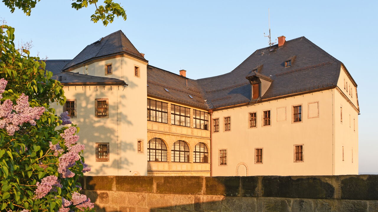 Die Georgenburg in der abendlichen Sonne mit einem Fliederstrauch und der Außenmauer im Vordergrund