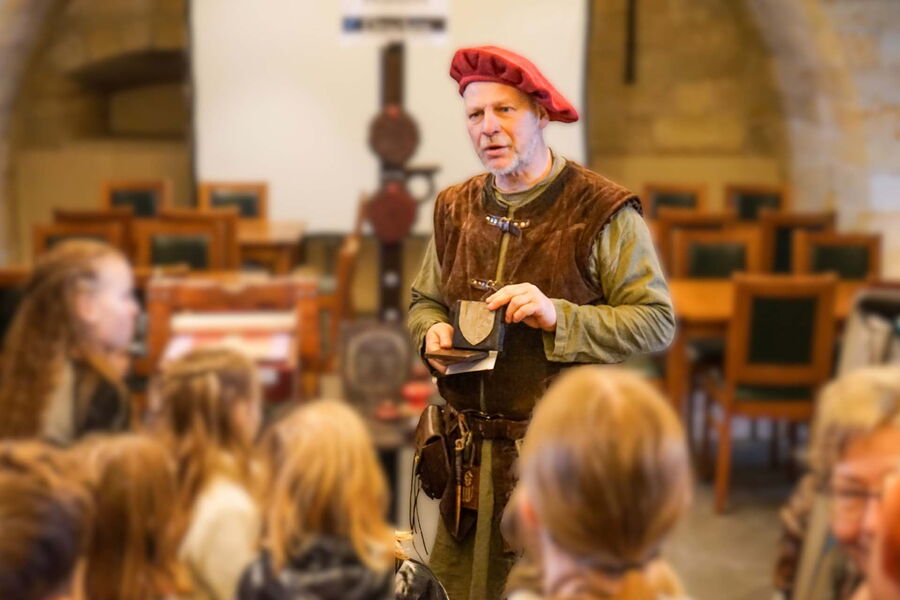 Ein historisch gekleideter Mann erklärt einer Gruppe von Kindern die Bedeutung der Alchemie in früherer Zeit