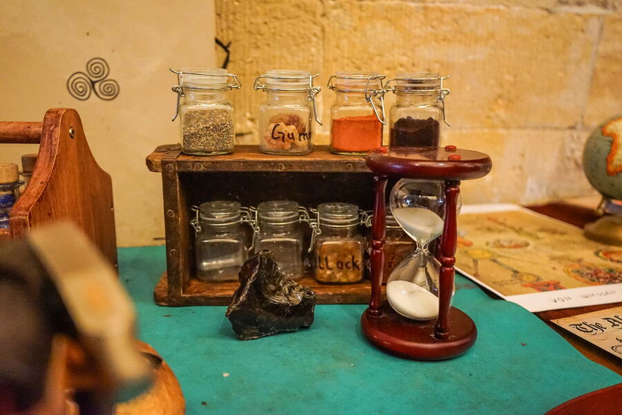 Gläser mit Pulvern und Granulaten in einem Regal, davor eine Sanduhr
